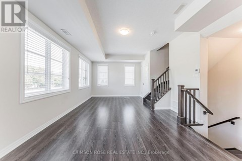A spacious room with wood flooring and a staircase.