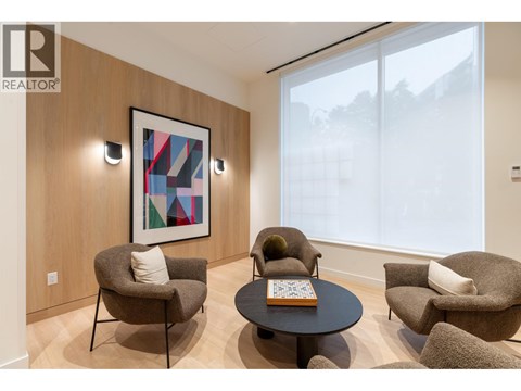 A living room with a large window, a round table, and a painting on the wall.