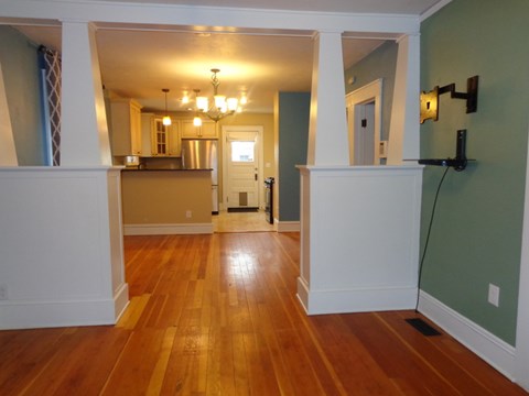 A room with wooden floors and a kitchen area in the background.