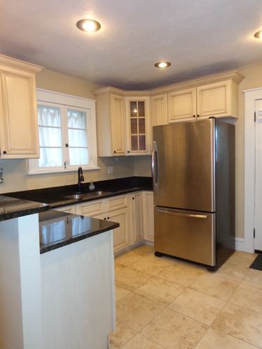 A kitchen with a black counter top and a stainless steel refrigerator.