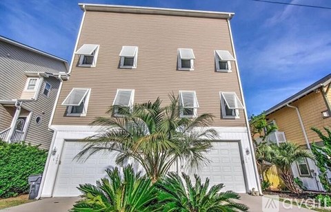 A two-story building with a garage and a palm tree in front.