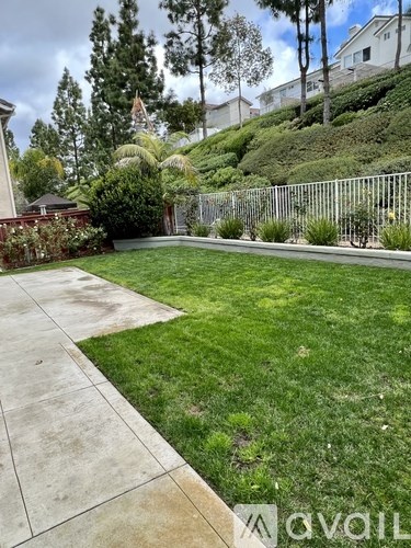 A backyard with a concrete walkway and a metal fence.