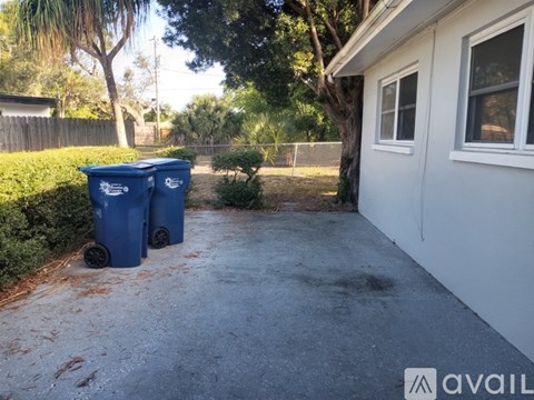 Two blue garbage bins are placed on a driveway in front of a house.