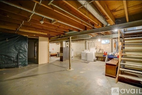 A large empty room with wooden beams on the ceiling and a white refrigerator in the corner.