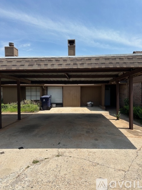 A covered patio area with a concrete floor and a trash can.