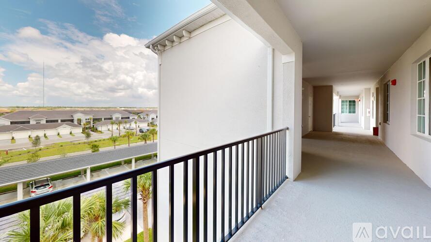 A balcony with a black railing overlooks a parking lot and other buildings.