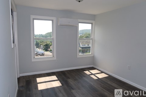 A room with two windows and wooden flooring is available for rent.
