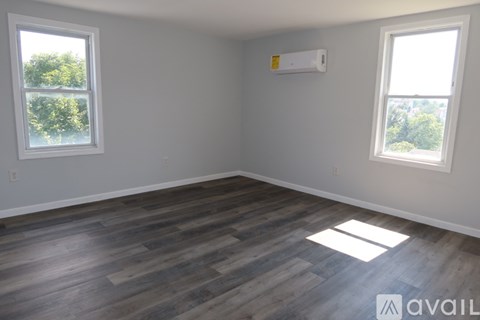 A room with wooden flooring and two windows.