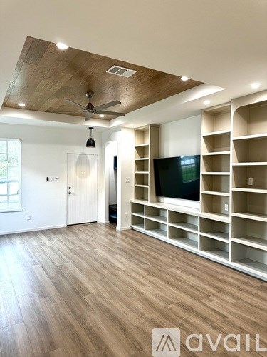 A spacious room with a wooden ceiling and floor, a television on a wall-mounted stand, and built-in shelving.
