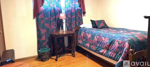 A bedroom with a bed, table, and a window with curtains.