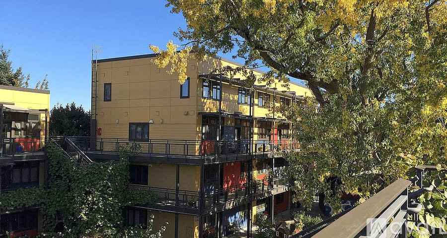 A yellow building with balconies is surrounded by trees.