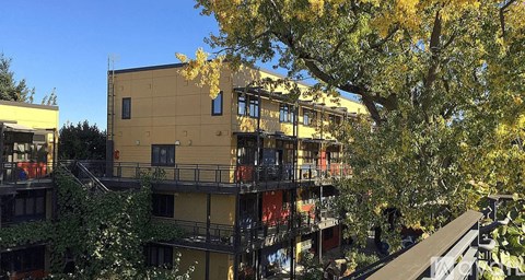 A yellow building with balconies is surrounded by trees.