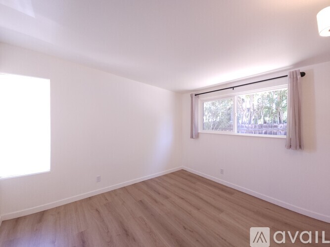 A room with wooden flooring and a window with a view of trees outside.