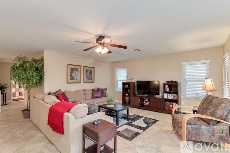 A living room with a white couch, a ceiling fan, and a television.
