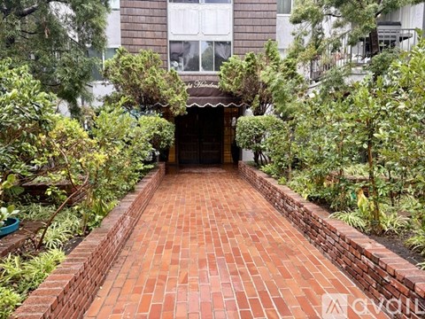 A brick pathway leads to a building entrance surrounded by greenery.