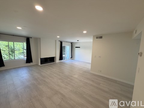 A spacious room with wooden flooring and a large window with black curtains.