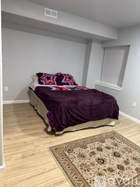 A bedroom with a bed covered in a purple comforter and a patterned rug in front of it.