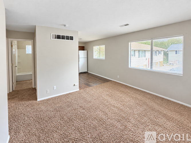 A large, empty room with a carpeted floor and a window showing a view of a house.