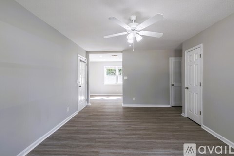 A spacious room with a ceiling fan and light, and a door leading to another room.