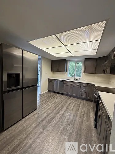 A kitchen with dark wood flooring and a refrigerator on the left.