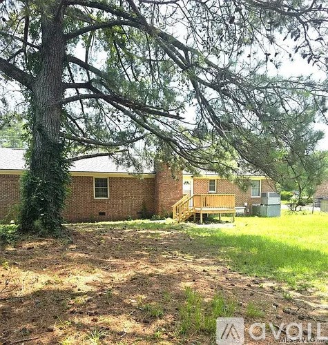 A tree in front of a house with a grassy area in front of it.