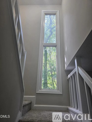 A window with a view of trees is in a room with white walls.