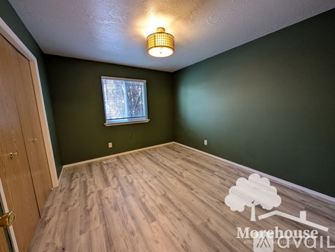 A room with a wooden floor and a window with a view of trees outside.