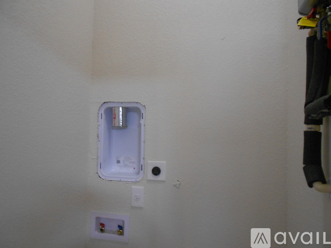 A white wall with a small square hole and a white box with a black handle.