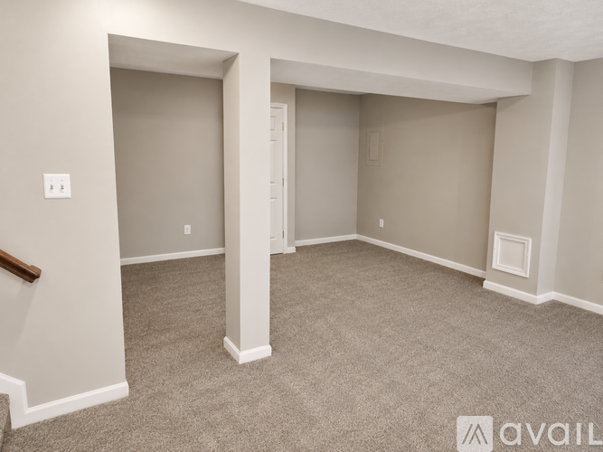 A spacious room with a carpeted floor and a staircase on the left side.