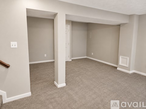 A spacious room with a carpeted floor and a staircase on the left side.