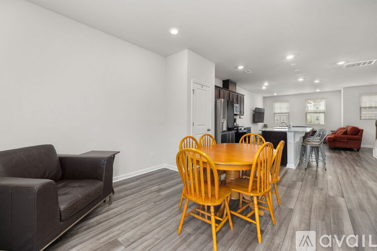 A living room with a brown couch, a wooden dining table with chairs, and a kitchen area in the background.
