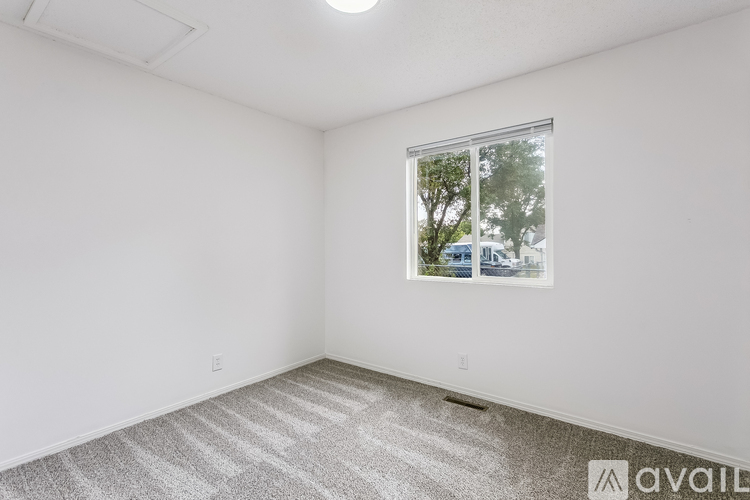 A room with a carpeted floor and a window showing trees and a building outside.