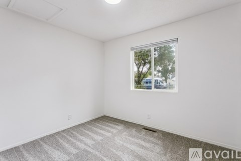 A room with a carpeted floor and a window showing trees and a building outside.