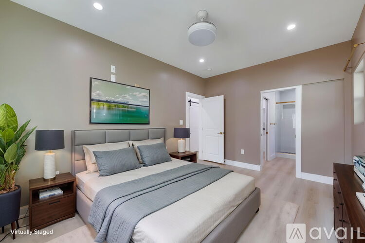 A bedroom with a large bed, a painting on the wall, and a plant on the nightstand.