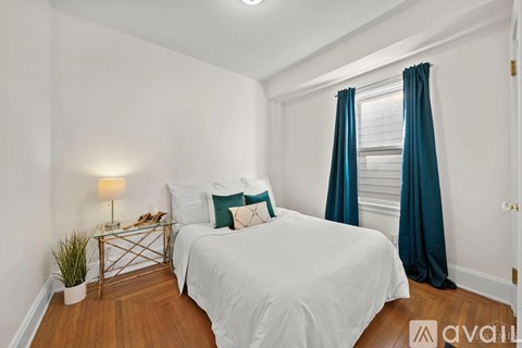 A bedroom with a white bed and a small table with a lamp and a plant on it.