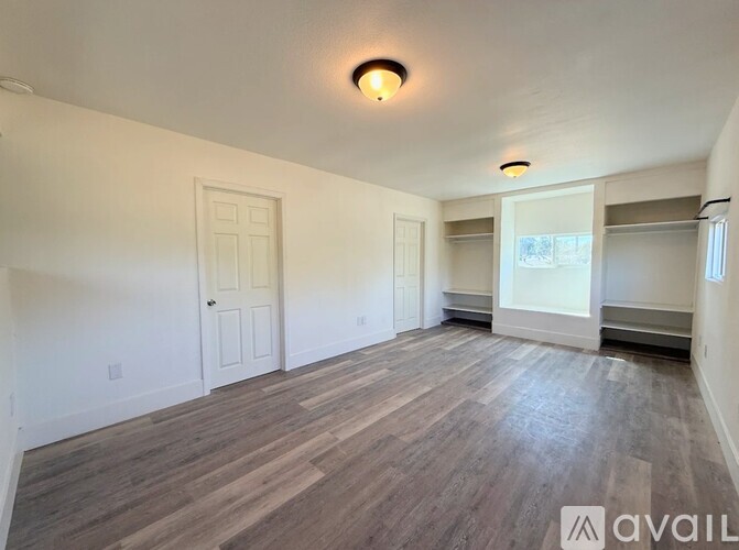 A spacious room with wooden flooring and white walls.