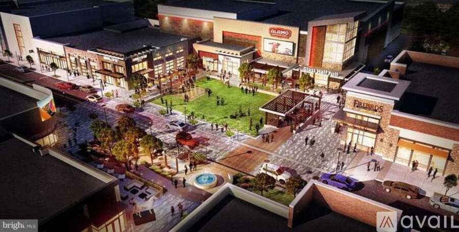 A brightly lit outdoor shopping area at night with a pool in the center.