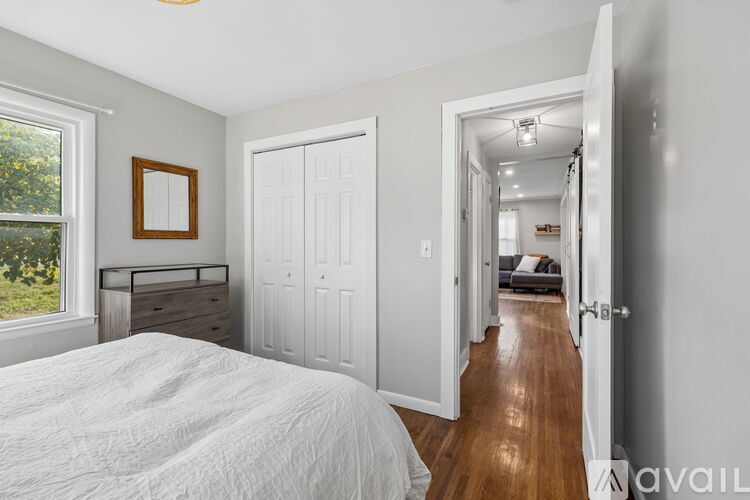 A bedroom with a white bed and a window with a view of trees.