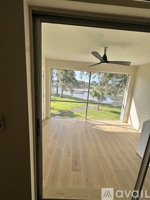A room with a ceiling fan and wooden flooring with a view of a grassy area outside.