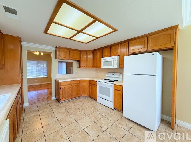 A kitchen with a white fridge, wooden cabinets and a tiled floor.