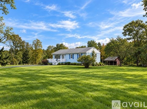 A house with a white porch and a red roof is surrounded by a grassy field.