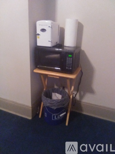 A white toaster oven and a white microwave on a wooden stand with a blue trash bag underneath.