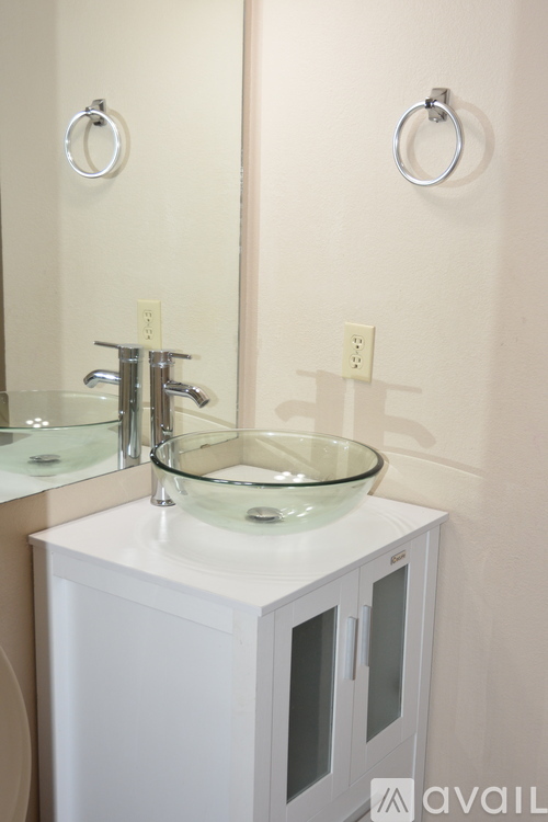 A bathroom with a white cabinet and a glass bowl sink.