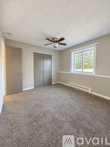 A room with a ceiling fan and a window with a view of trees.