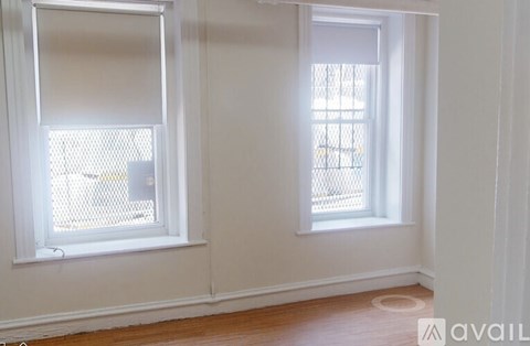 Two windows with white frames and white blinds in a room with wooden floors.