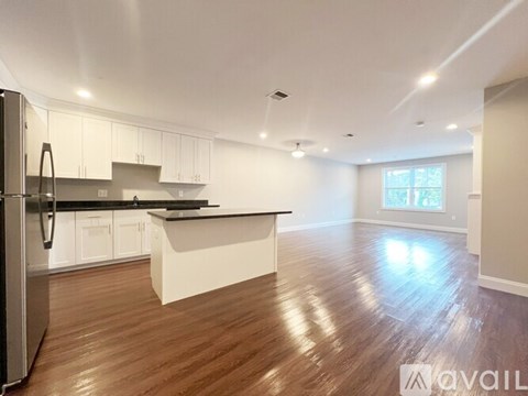 A kitchen with white cabinets and a black countertop with a refrigerator on the left.