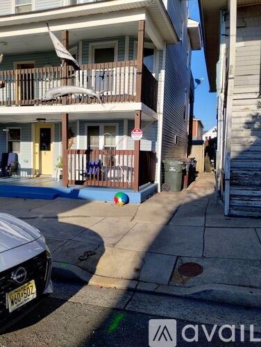 A white car is parked on the street in front of a building with a balcony.