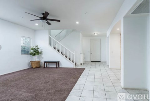 A living room with a brown carpet and a ceiling fan.