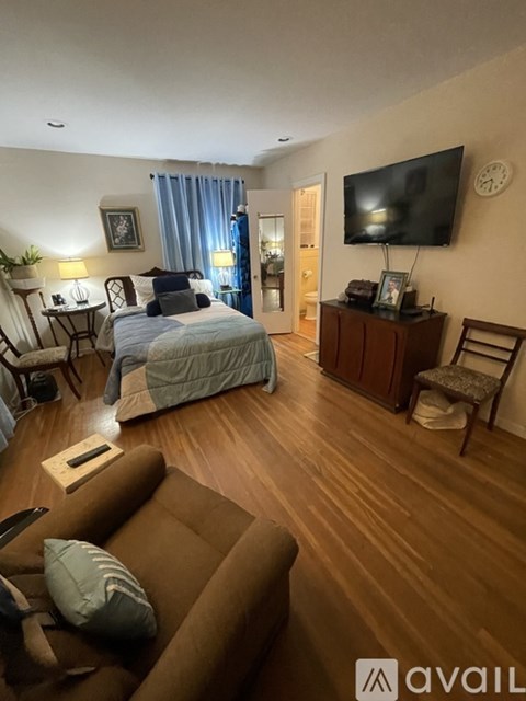 A bedroom with a bed, a couch, a chair, a cabinet, a television, and a clock on the wall.