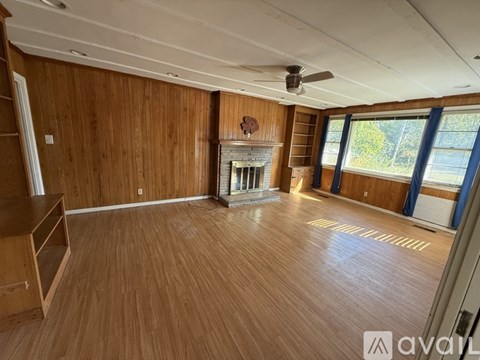 A spacious room with wooden walls and flooring, a fireplace, and a ceiling fan.